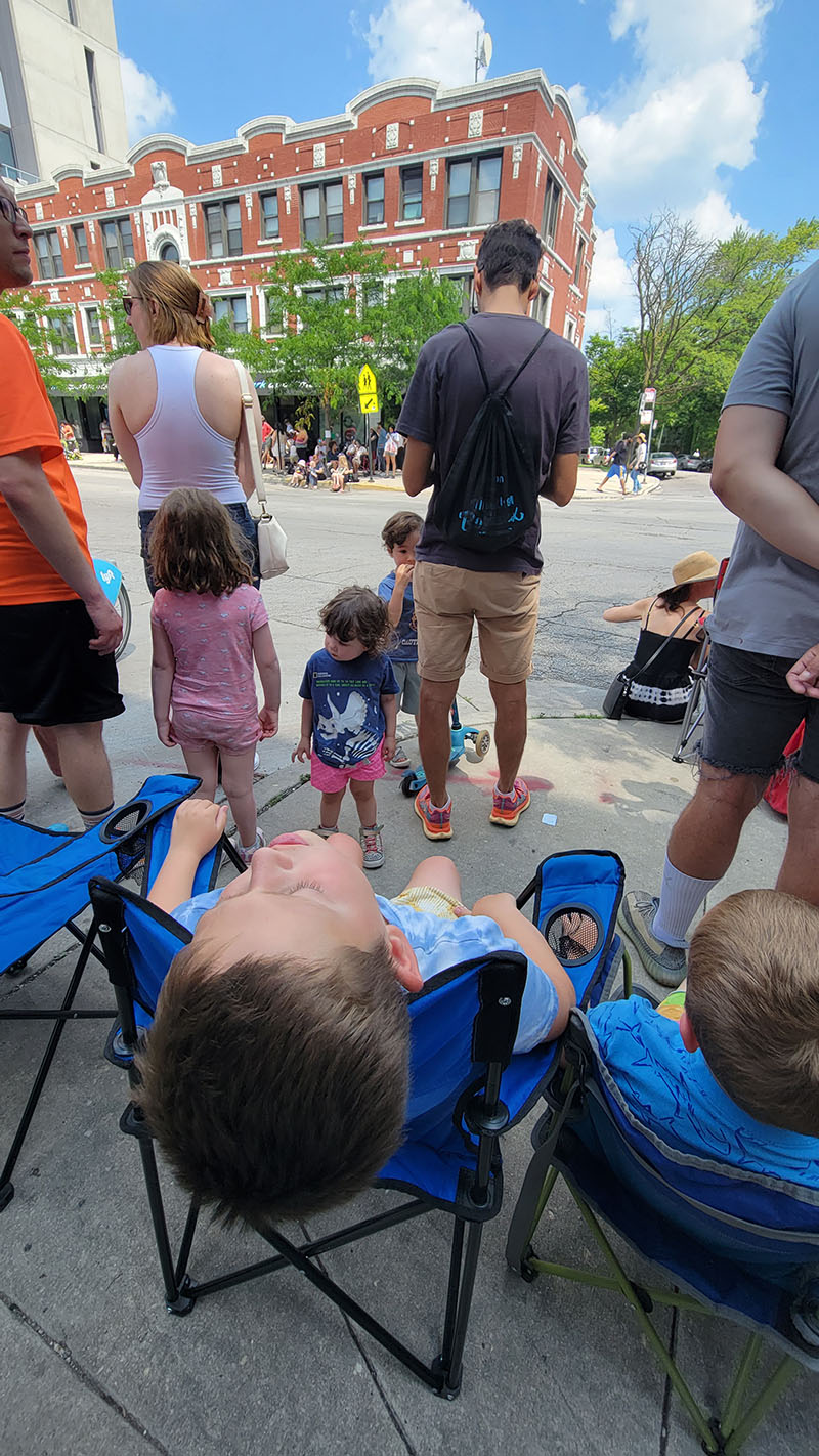 Overheating kids in lawn chairs at the 4th of July picnic with Quinn's old apartment building in the background