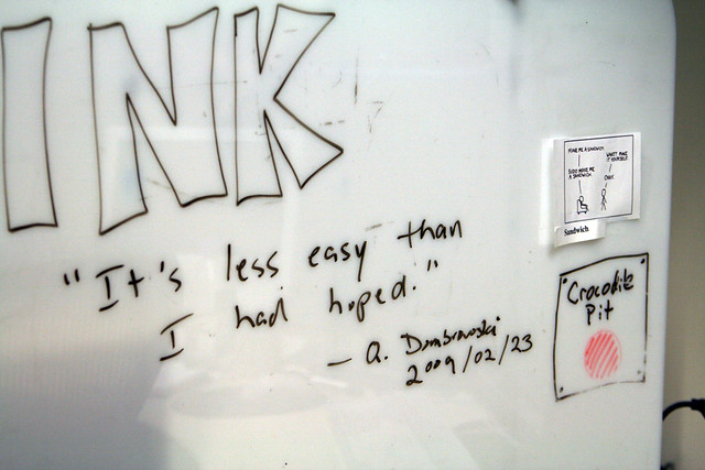 A photo of a whiteboard with a drawing of a crocodile pit, an xkcd comic taped up, and the quote "It's less easy than I had hoped" attributed to Q Dombrowski
