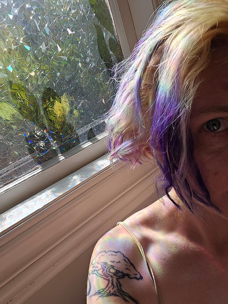 Quinn with bleached hair, only purple on the ends, standing by the window