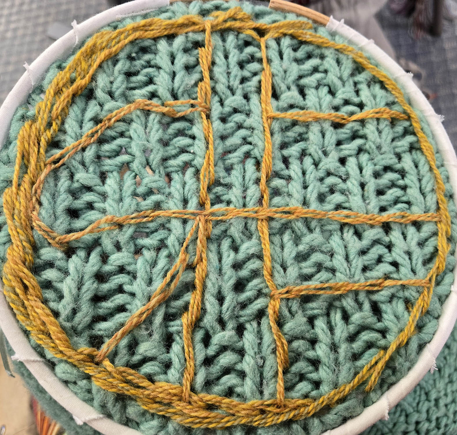 Yellow yarn on a green sweater with a circular sigil reading 'choose'